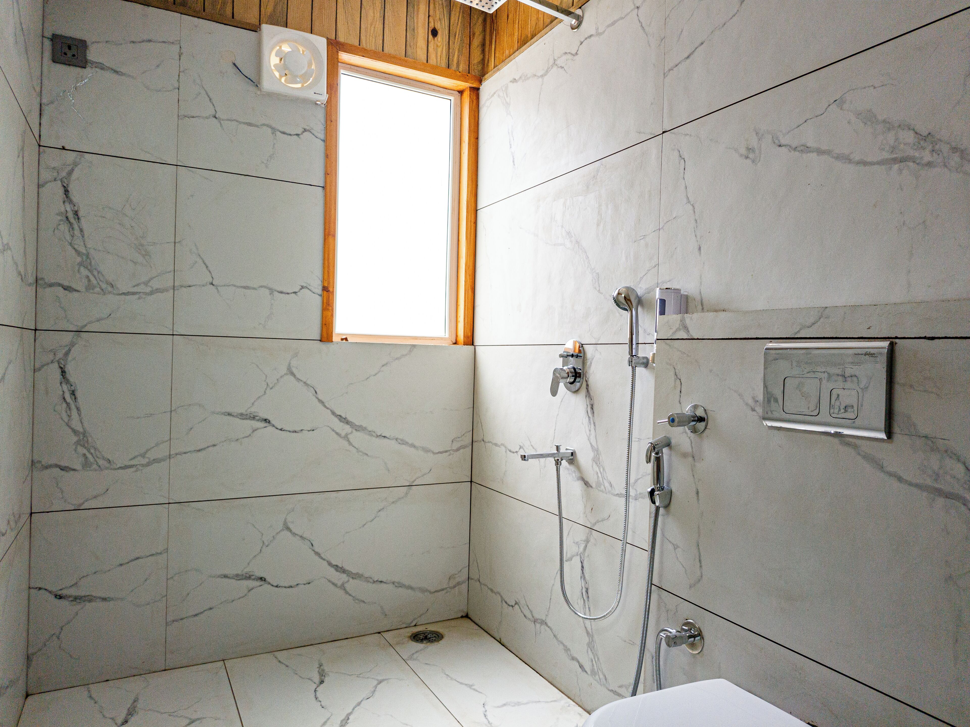 A bathroom with marble walls, a window, and a shower with multiple controls.