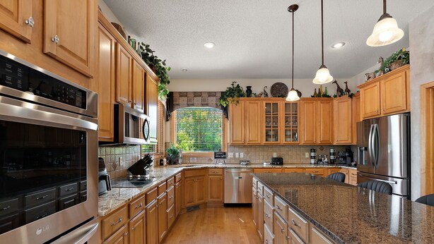 A modern kitchen with wooden cabinets, stainless steel appliances, granite countertops, and pendant lighting.