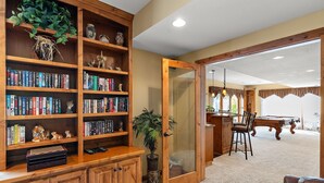 A room with a wooden bookshelf filled with books, a billiards table, and a door leading to another room.