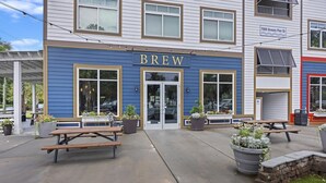 A building with a blue exterior and the word "BREW" prominently displayed. There are outdoor seating areas with tables and chairs, and potted plants around the entrance. - Charming Cottage-resort style pool, pickleball (Hanahan)