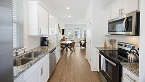 A modern kitchen with white cabinets, granite countertops, stainless steel appliances, and a dining area with a table and chairs. - Charming Cottage-resort style pool, pickleball (Hanahan)