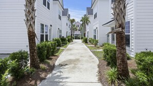 A row of white single-story houses with a central concrete pathway, surrounded by palm trees and small shrubs. - Charming Cottage-resort style pool, pickleball (Hanahan)