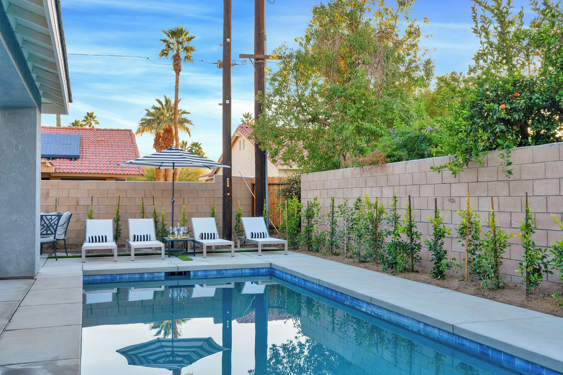 A backyard with a swimming pool, white lounge chairs, and a brick wall.