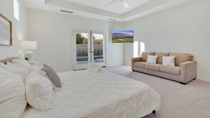 Un dormitorio con una cama grande, un sofá color crema, un ventilador de techo y un televisor en la pared.