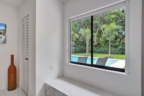 A bathroom with a large window overlooking a swimming pool and lush greenery.