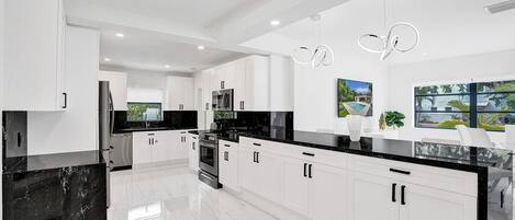 A modern kitchen with white cabinets, black countertops, and a central island.