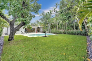 A backyard with a swimming pool, a house, and surrounding greenery.