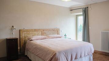 Un dormitorio con cabecera de madera, cama con ropa de cama rosa, mesita de noche, lámpara y ventana con cortinas.