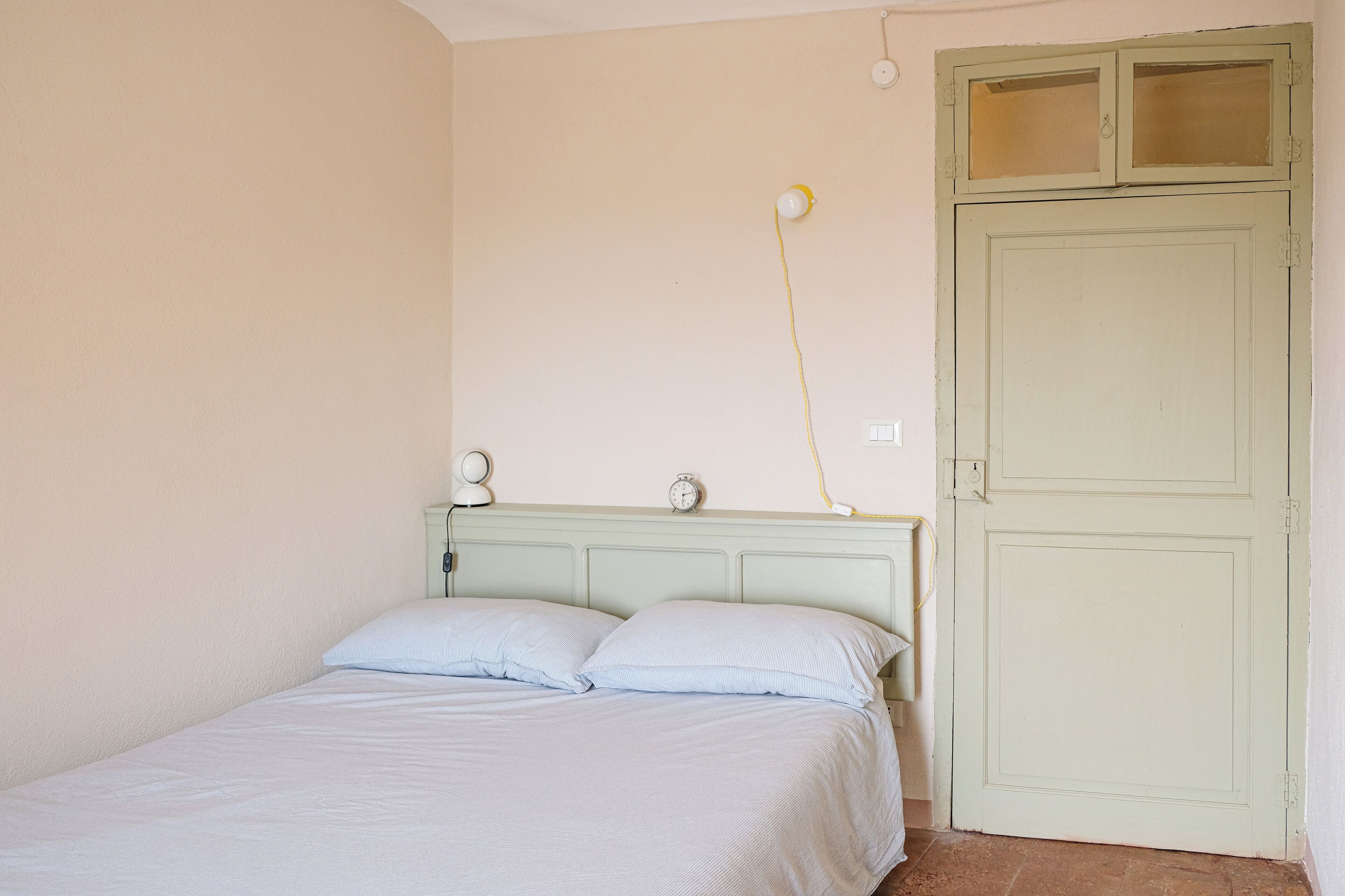 A bedroom with a bed, a nightstand, a wall-mounted lamp, and a door.