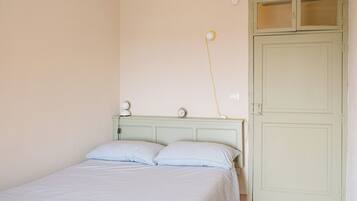 A bedroom with a bed, a nightstand, a wall-mounted lamp, and a door.
