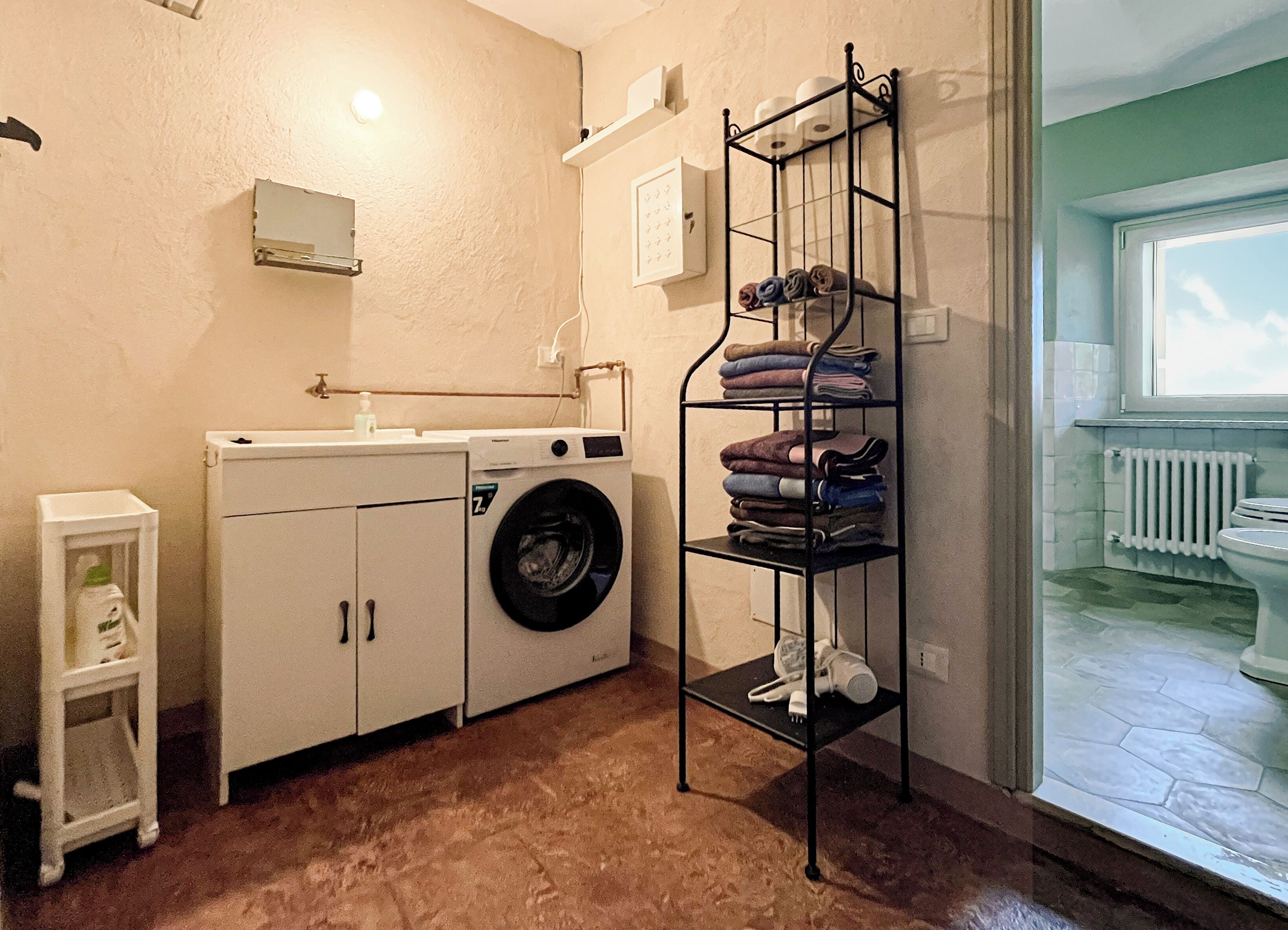 A laundry room with a washing machine, a drying rack, and a small shelf with folded towels.