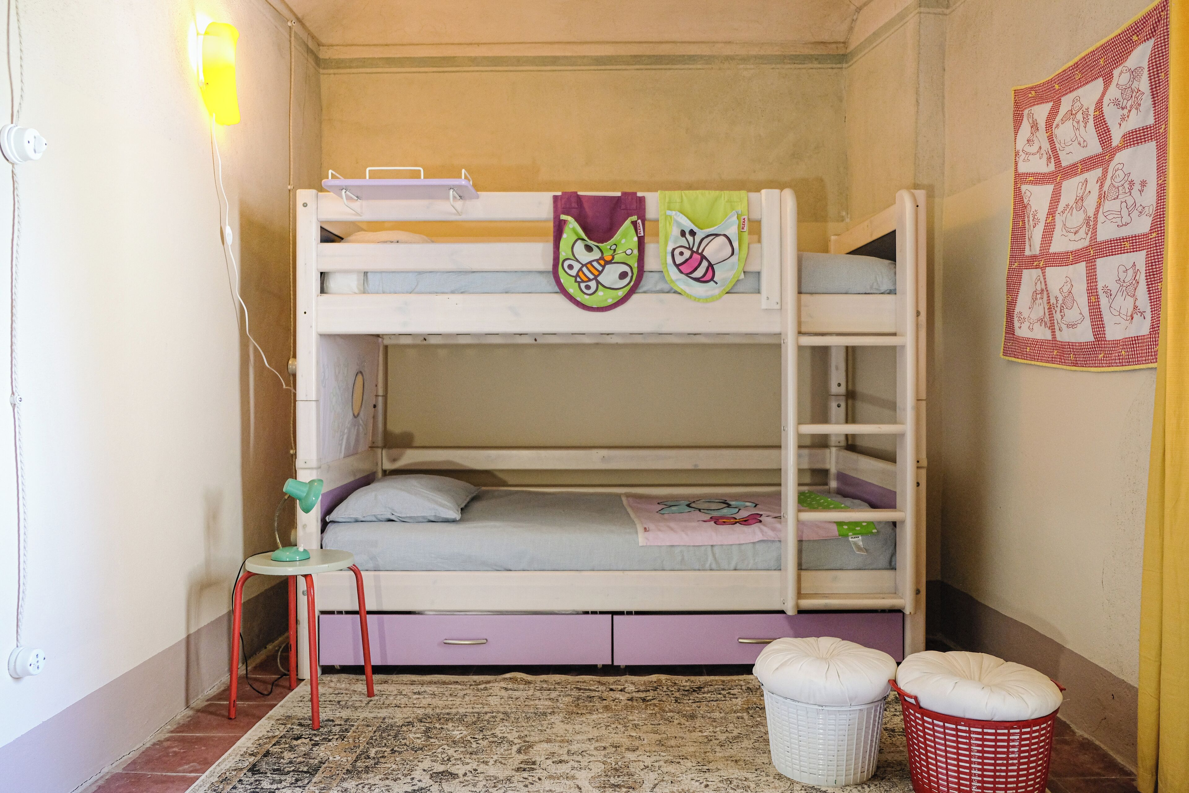 Una cama litera con escritorio y silla, una mesita pequeña y un panel decorativo en la pared.