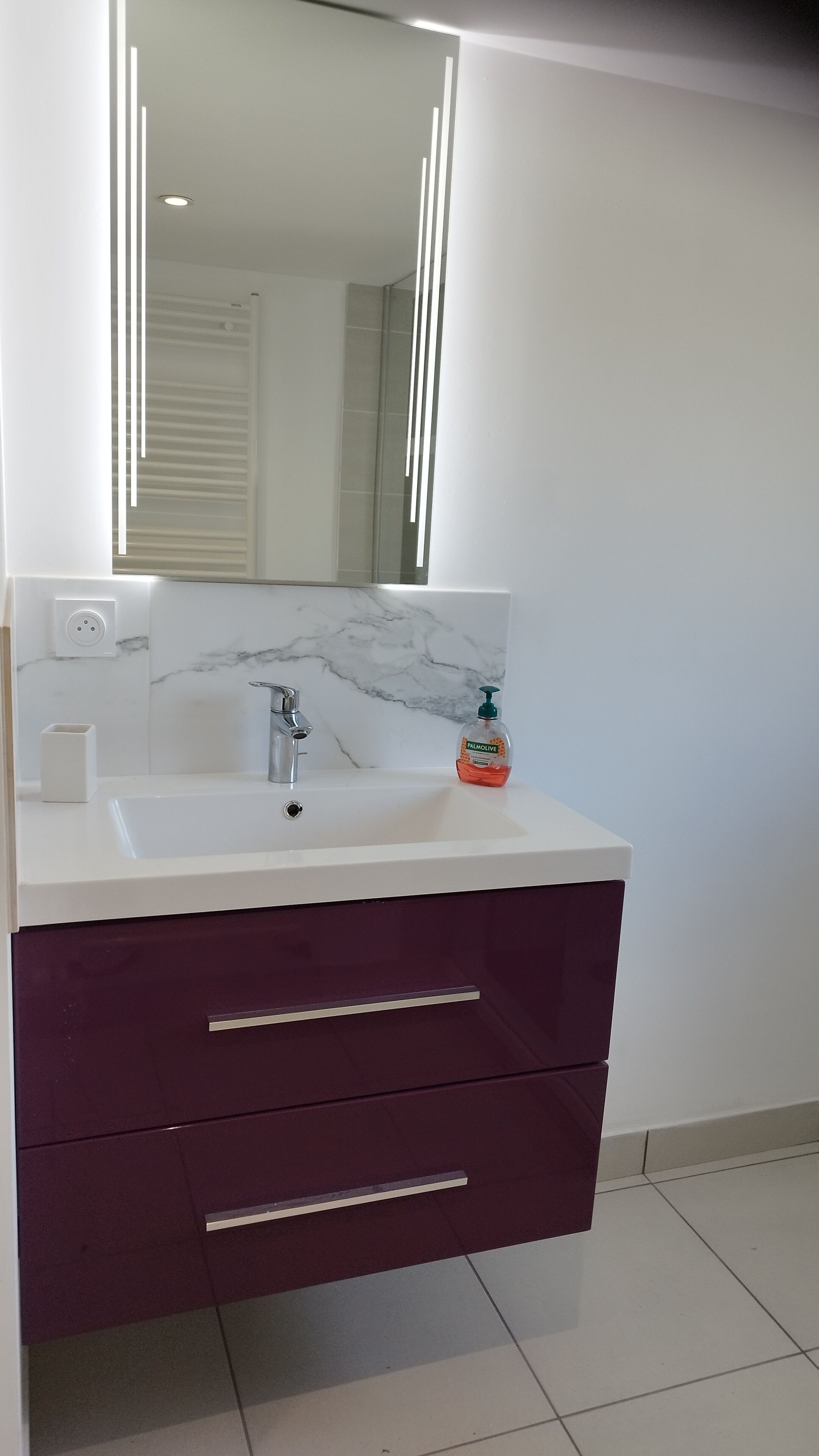 A modern bathroom with a white sink, marble backsplash, and a purple vanity with drawers.