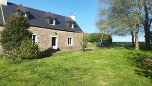 A stone house with a sloped roof, a small garden, and a parked car. - Gite Lann er Viline (Camors)