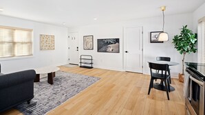 Ein modernes Wohnzimmer mit einer Couch, einem Esstisch mit Stühlen, einem Teppich und Kunstwerken an den Wänden.