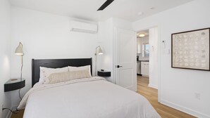 Ein modernes Schlafzimmer mit einem großen Bett, Nachttischlampen, einem Deckenventilator und einer durchgehenden Tür erkennbaren Küche.