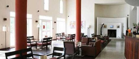A spacious lobby with high ceilings, large windows, and a central seating area with tables and chairs.