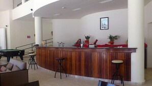 Zona de recepción con mostrador de madera, dos taburetes tipo bar, una mesa de billar y un cuadro en la pared.