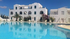 Un edificio moderno con piscina, que presenta fachada blanca, ventanas arqueadas y un balcón.