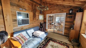 A cozy cabin interior with a blue sofa, a fan, a chandelier, and a large window. - Spacious, modern, home by the lake! (Northville)