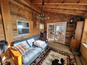 A cozy cabin interior with a blue sofa, a fan, a chandelier, and a large window. - Spacious, modern, home by the lake! (Northville)