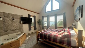 A bedroom with a bed, a window, a plant, and a bathroom with a bathtub and sink. - Spacious, modern, home by the lake! (Northville)