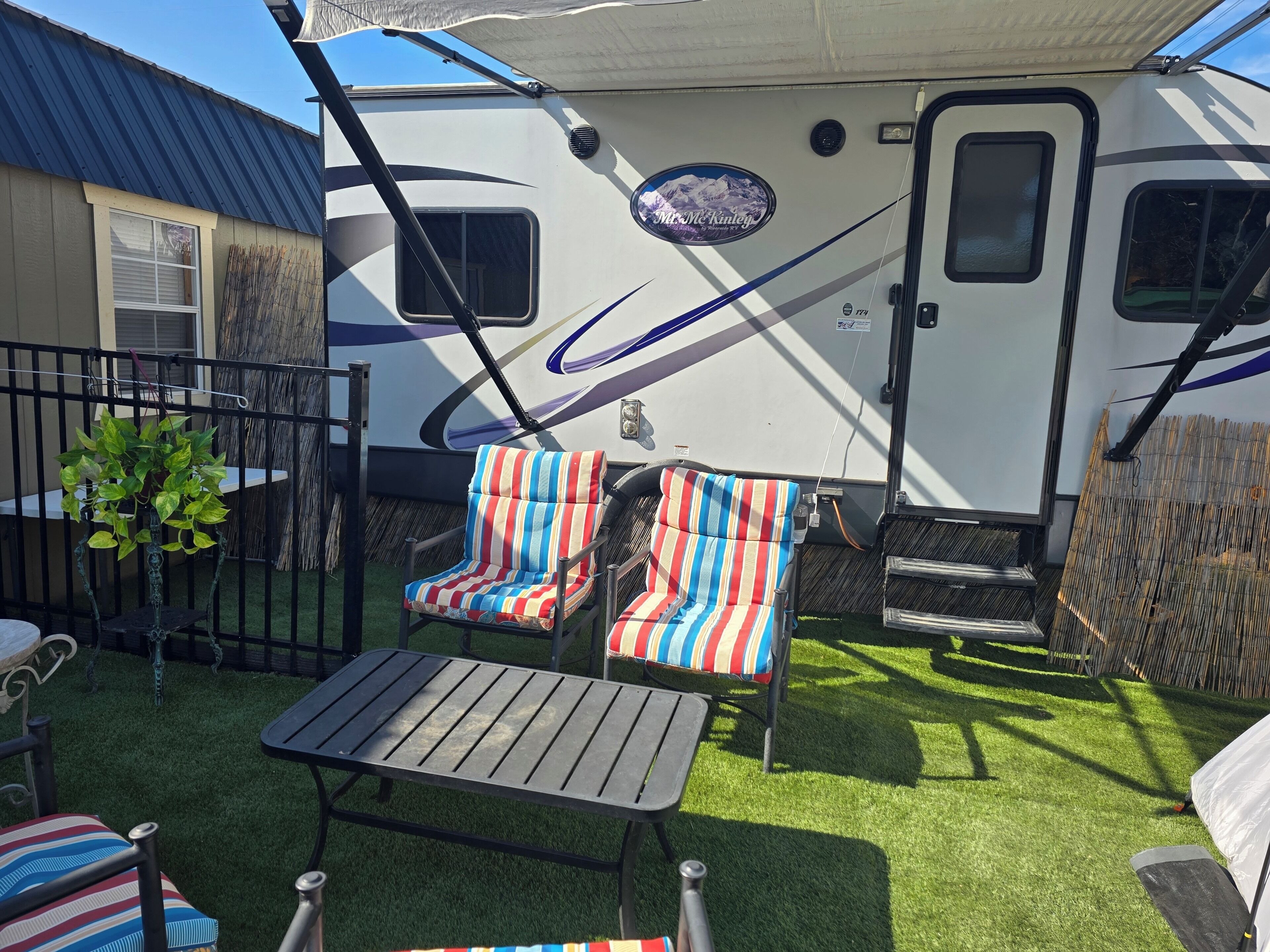 A recreational vehicle with striped chairs and a table in a backyard.