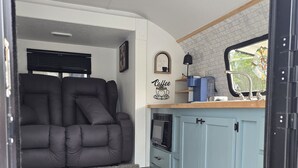 Ein kompakter Wohnraum mit einer Couch, einer Küchenzeile inklusive Schränken, einer Mikrowelle und einer Wanddekoration zum Thema Kaffee.