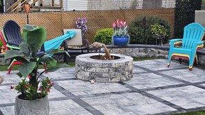 Eine Terrassenfläche mit Feuerstelle, Gartenmöbeln und Pflanzkübeln.