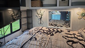 Ein Schlafzimmer mit einem großen Bett, einem Fenster, einem Spiegel und einem an der Wand befestigten Regal mit Körben.