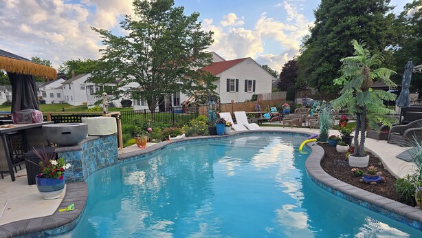 Ein Pool mit Fliesenrand, umgeben von Kübelpflanzen und Gartenmöbeln.