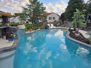 Une piscine dont le bord est revêtu de carrelage, entourée de plantes en pot et de mobilier d’extérieur.