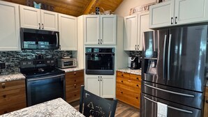 A modern kitchen with white cabinets, stainless steel appliances, and a marble countertop.
