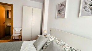 A bedroom with a bed, pillows, a chair, a wardrobe, and two framed floral artworks on the wall.