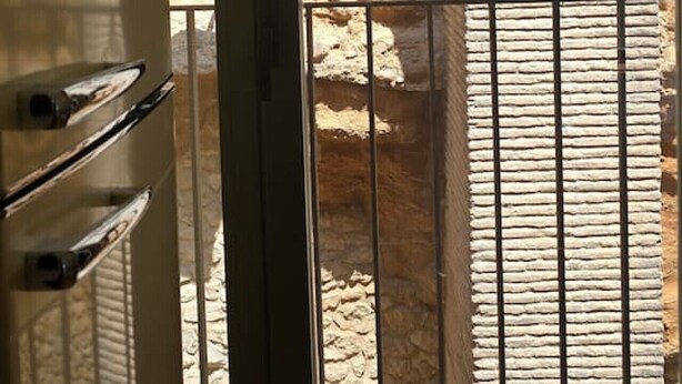 A view through a window with a stone wall and a metal railing.