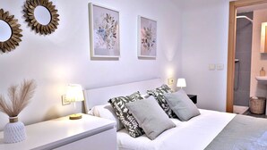 A hotel room with a bed, two bedside tables, a nightstand, a wall-mounted mirror, and two framed floral artworks.