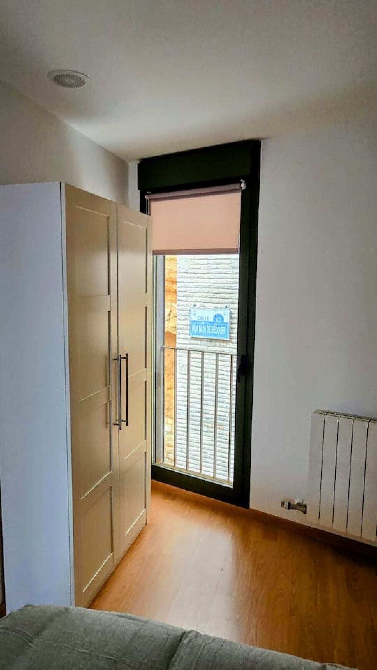A room with a wardrobe, a radiator, and a window with blinds.