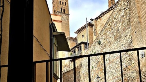 A balcony with a view of a historic stone wall and a tower.