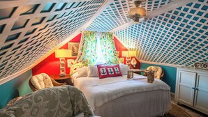 Ein Schlafzimmer mit schrägen Wänden, einem Bett mit weißer Bettdecke, zwei Nachttischlampen, einem Nachttisch und einem Sessel.