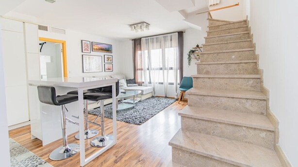 Uma sala de estar moderna com escada, área de jantar e cozinha.