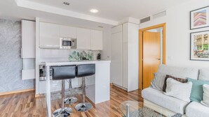 Um apartamento moderno com cozinha, dois bancos altos, um sofá e uma mesa de centro de vidro.