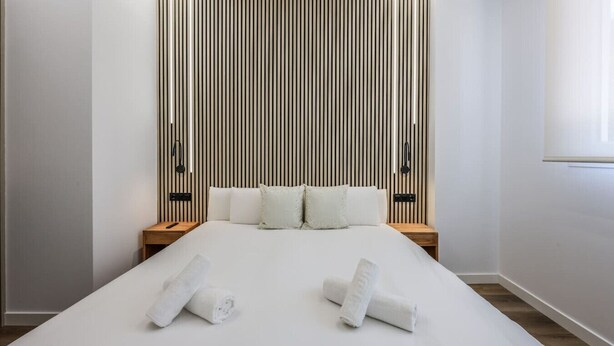 Ein modernes Schlafzimmer mit einem großen Bett, zwei Nachttischen und einer Wandpaneinung aus Holz.
