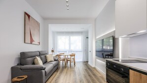 Eine moderne Küche mit Einbauherd, Holzschränken und einem Essbereich inklusive grauer Couch und Holzsesseln.
