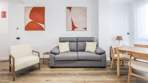 Ein modernes Wohnzimmer mit grauem Sofa, einem weißen Sessel und einem Holzes Esstisch.