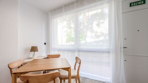 Ein Zimmer mit einem Holztisch, Stühlen, einer Lampe und einem Fenster mit durchsichtigen Vorhängen.