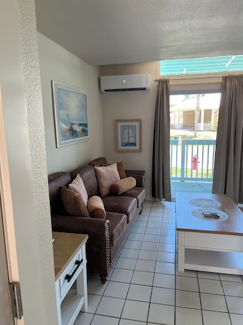 A living room with a brown leather sofa, a white table, and a view of a blue outdoor area with a railing.