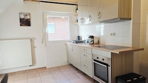 Cocina compacta con armarios blancos, horno empotrado y ventana que proporciona luz natural.