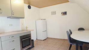 Una cocina compacta con estufa, horno y refrigerador. Hay una mesa de comedor con sillas y un reloj en la pared.