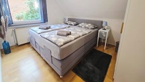 Un dormitorio con cama, mesita de noche, lámpara, ventana con cortinas y radiador.