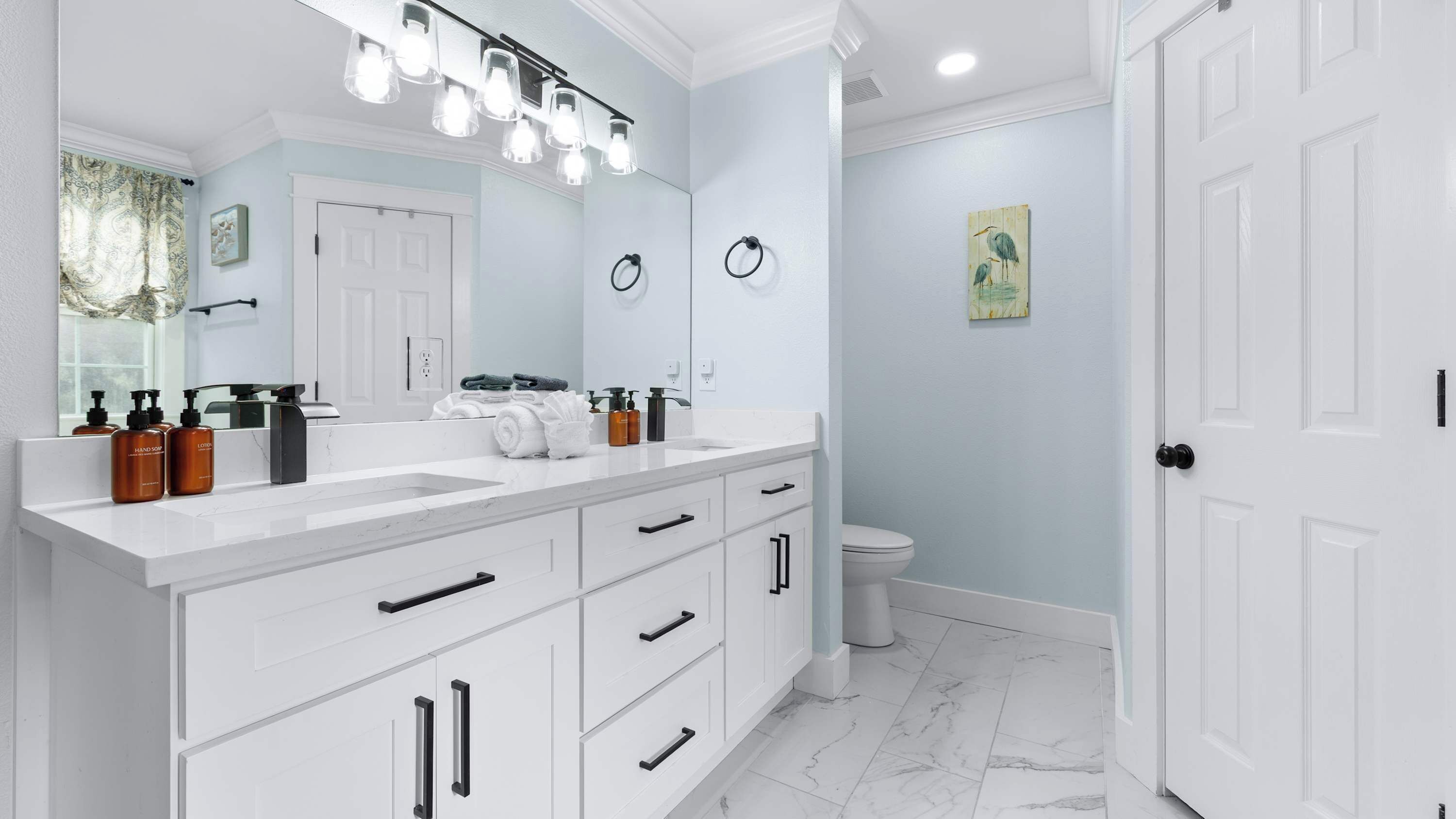 A modern bathroom with white cabinetry, a large mirror, and a light blue wall.